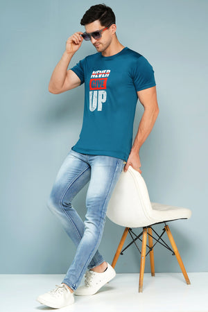 Man wearing a blue t-shirt with text and light blue jeans, standing against a light gray background.