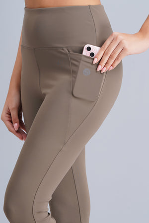 Brown pants with a pocket and a phone being placed inside on a light gray background