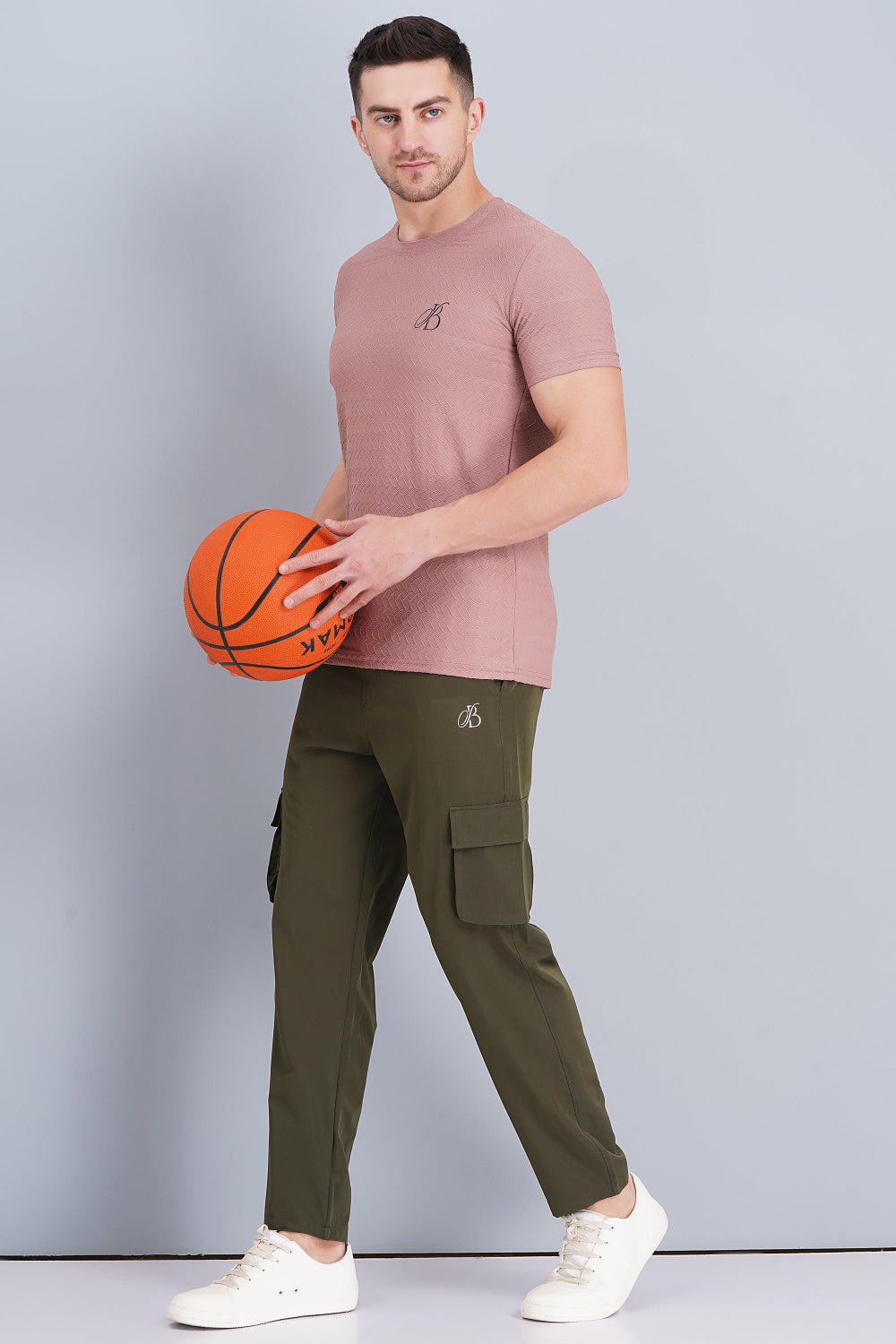 Man holding a basketball wearing a pink t-shirt and green cargo pants on a gray background